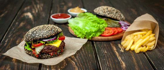 black-hamburger with lettuce, tomatoes and fries. Wooden background