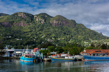 Fototapeta na wymiar Mahe, Seychelles - Oct 26th 2018 - Fisherman boats in the Mahe's port in Seychelles with mountains covered with green vegetation in the background