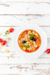 Minestrone, vegetarian soup with pasta and vegetables on white wooden rustic background. Traditional italian food. Top view