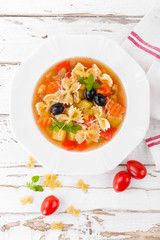 Minestrone, vegetarian soup with pasta and vegetables on white wooden rustic background. Traditional italian food. Top view