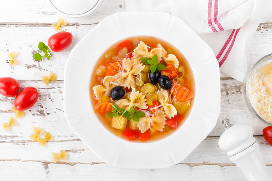 Minestrone, vegetarian soup with pasta and vegetables on white wooden rustic background. Traditional italian food. Top view
