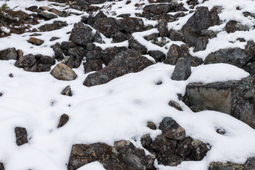 Stones on the mountainside covered with snow. Background of stones and snow.