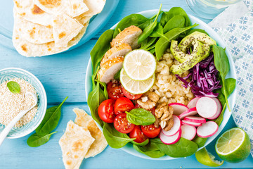 Bowl with grilled chicken meat, bulgur  and fresh vegetable salad of radish, tomatoes, avocado, kale and spinach leaves. Healthy and delicious summer lunch. Top view