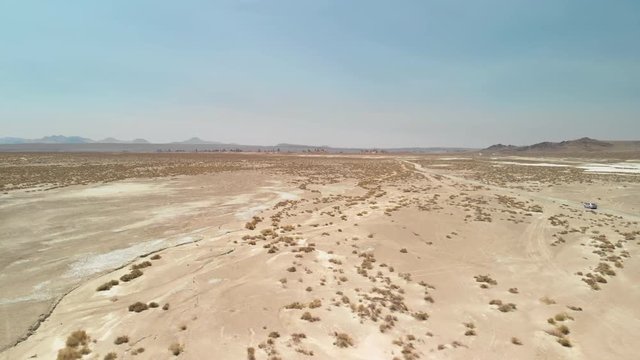 Drone shot of a desert landscape with small shrubs and rocky mountains in the far distance 