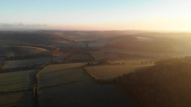 Aerial shot of a beautiful golden sunset over rolling green hills and farmland in the Chiltern Hills, United Kingdom.