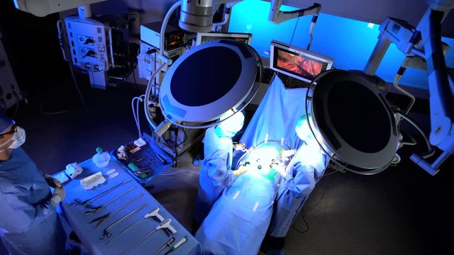 View overhead of Laparoscopy surgical training operation transmitted on hospital monitor performed by Caucasian male and female wearing surgical gloves and protective clothing