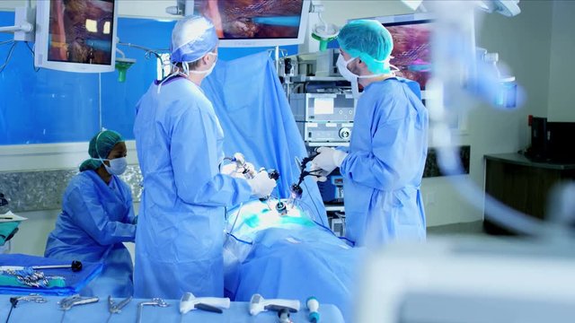Laparoscopic surgical operation transmitted on hospital video monitors being performed by Caucasian surgeons using an Endoscopy and surgical tools while wearing protective clothing 