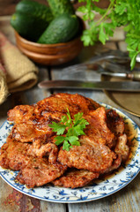 Freshly fried pork neck on a plate on a wooden background. Cucumbers in the background
