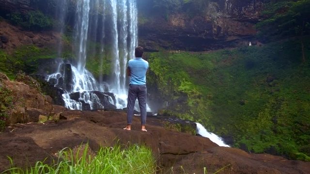 backside guy stands on rock watches powerful waterfall