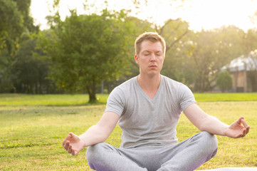 Fototapeta premium Young handsome man closing eyes while meditating at the park