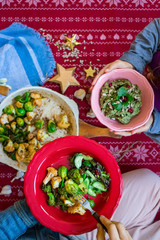 Christmas lunch, dinner food. Baked, roasted or grilled vegetables in cast iron skillet. Brussels sprout, cauliflower. Woman hands eat, take food from red plate or bowl. Hold on legs