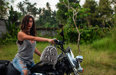 Fototapeta na wymiar A woman sitting on a bike near fantastic landscape, jungle, tropical forest in front of her and the nature.Concept of style, fashion in adventure and travel with python accessory