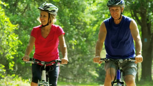 Healthy Caucasian American seniors enjoying bike ride outdoors in the forest 