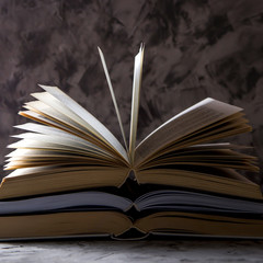 A stack of open books with flipped pages on a gray background. Learning reading and self-development concept