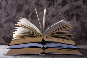 A stack of open books with flipped pages on a gray background. Learning reading and self-development concept