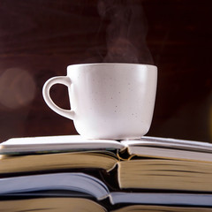A white cup with tea is on the open pile of books. Learning, reading and love of literature concept
