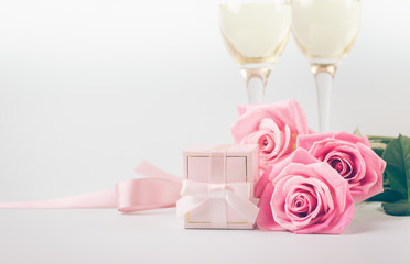 Pink roses, a gift with a silk ribbon and glasses on a light pastel background. Delicate bouquet and a gift for a solemn event. Selective focus. Copy space.