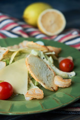 Fresh caesar salad with shrimps in a green plate on a light wooden table
