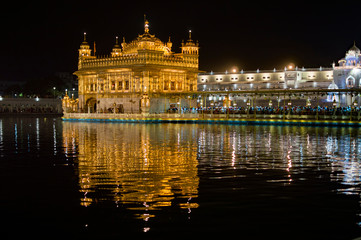 Fototapeta na wymiar Colorful and illuminated golden temple and its reflection
