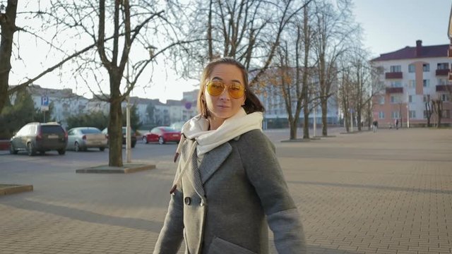 A young elegant girl in a gray coat and yellow goggles walks through the streets in the Sunny autumn weather in the evening. Stedicam slow-motion shot