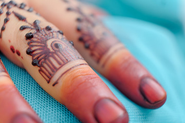 Image detail of henna being applied to hand over turquoise fabric. Selective focus.