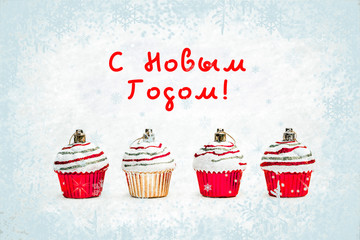 New Year greeting card - Christmas bauble cupcakes on white snow with snowflakes background. Russian translation: Happy New Year.