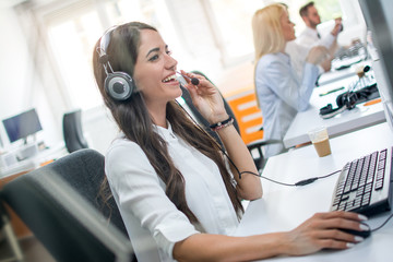 Portrait of call center worker accompanied by her team. Smiling customer support operator at work.