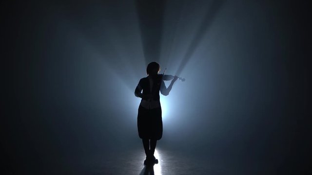 Girl plays the violin a classic composition in a dark smoky room. Silhouette. Black smoke background