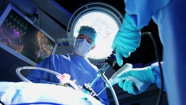 Medical Caucasian surgical team in scrubs performing Laparoscopy surgery on the patient in operating theatre using video camera technology 