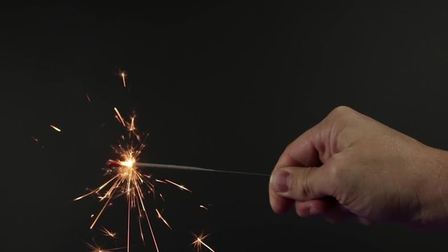 Man hand holding a small firework on black background until it stops. Hand moves away from screen. Actual firework sound