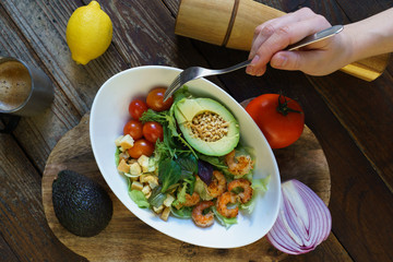avocado shrimp salad on wooden board  with fork and hand