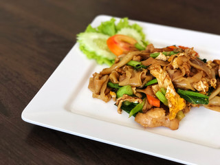 Fried noodle with soy sauce and pork, and Vegetable, tomato in white dish on the black table , Delicious and Street food, Thai Traditional And Popular Food