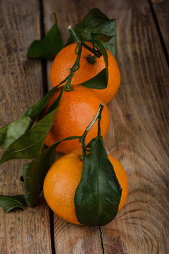 Three fresh tangerines with leaves on a wooden table