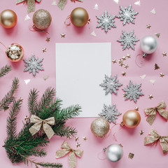 New Year's composition of a wish list and gold and silver ornaments, fir branches and candles on a pink background