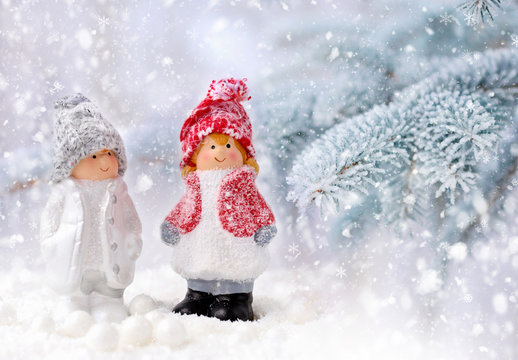 Christmas decorations little figure boy and girl on a background snow-covered fir branches. Christmas or New Year greeting card.