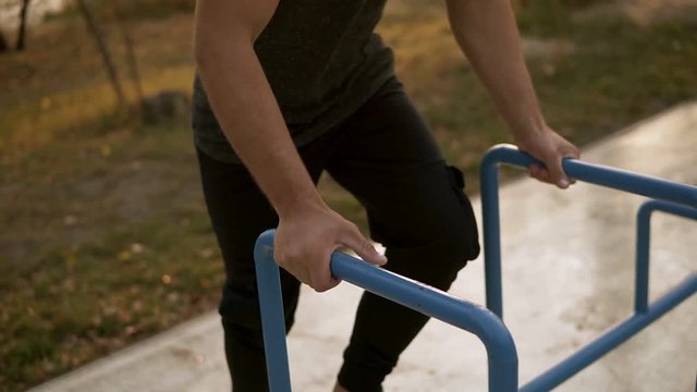 Young handsome man performing handstand on parallel bars outdoors. Beautiful head down position, perfect balance. Morning, trees on the background