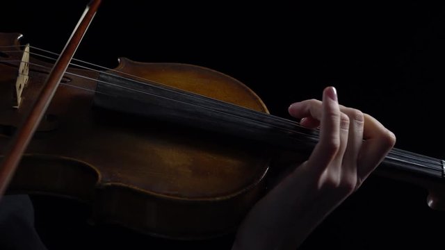 Women play strings of a violin in a dark room. Black background. Close up