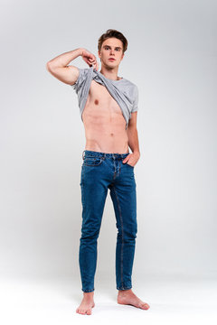 Perfect Torso. Handsome Young Man Taking Off His T-shirt And Looking At Camera While Standing Against White Background