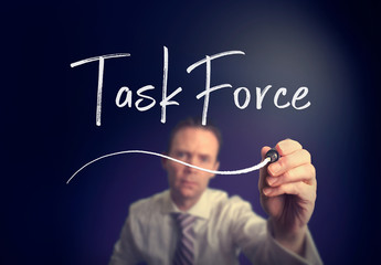 A businessman writing a Task Force concept with a white pen on a clear screen.