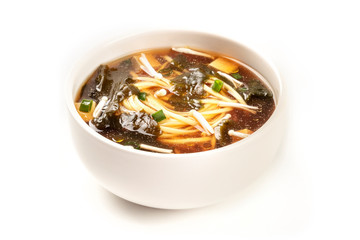 A photo of a bowl of miso soup with tofu, scallions, noodles, wakame, and enoki mushrooms, on a white background with a place for text