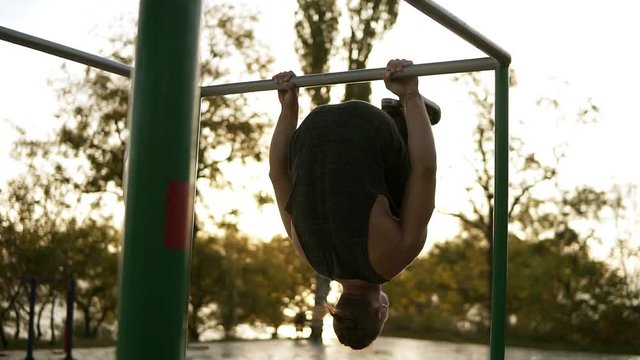 Young man doing exercises outdoors on horizontal bar outdoors. Calisthenics workout on paralel crossbar hanging on arms in horizontal position