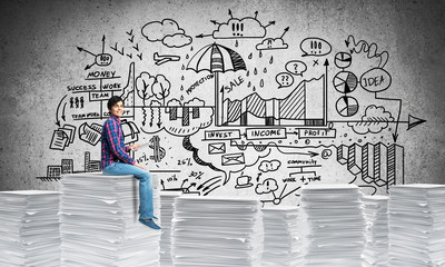 Attractive man sitting on pile of paper documents.