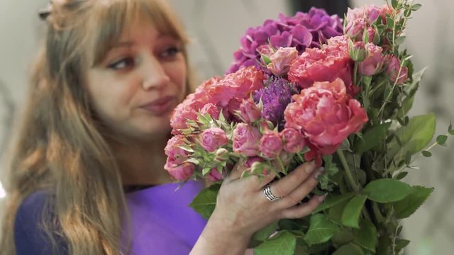 Lovely young woman florist sniffing a beautiful bouquet of flowers. Pretty girl holding a bunch of flowers at flower shop. European floral shop. Bouquet of beautiful Mixed flowers in woman hand