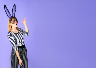 Seductive girl in black lace rabbit mask shows finger blank space for advertising. Beautiful sexy blonde woman in striped clothes in rabbit mask. Halloween, Christmas, New Year, Easter bunny costume.