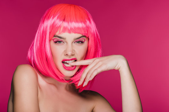 fashionable naked girl in neon pink wig biting finger, isolated on pink