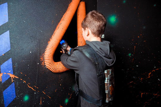 Excited kids and theirs parents aiming laser guns at other players during lasertag game in dark room