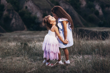 Fototapeta na wymiar Cute little sisters in white dresses hugging and kissing