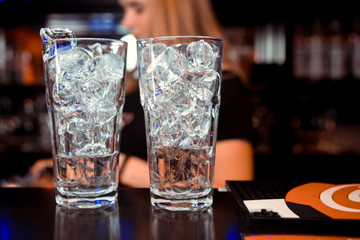 Barman pouring fresh alcoholic drink into the glasses with ice cubes on the bar counter