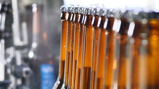 Brewery concept. Beer factory. Automatic Beer Bottling Line. Queue of ready filled bottles on the conveyer. 4k
