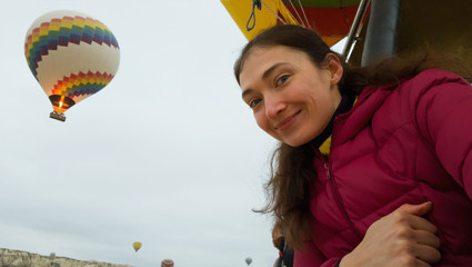 Brunette girl takes a selfie on the background of a flying balloon. A girl in a warm jacket flying in a balloon in Cappadocia. Happy traveler